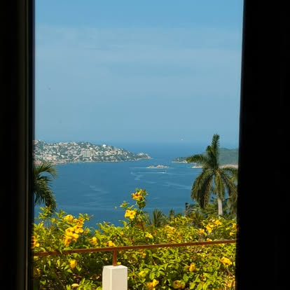 Acapulco Bay framed by a window and flowering plants at El Refugio